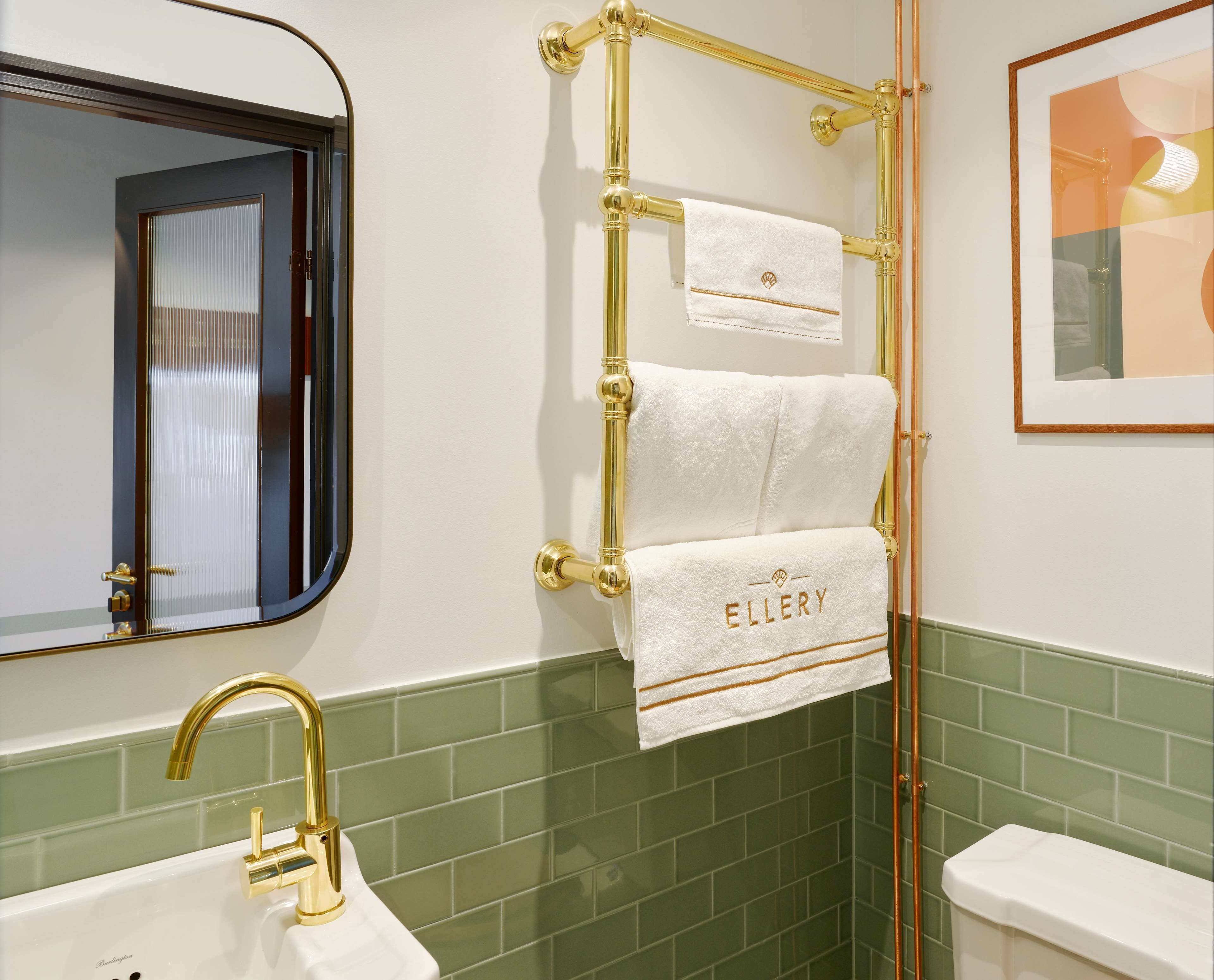 Ein Badezimmer mit goldenem Wasserhahn, einem Handtuchhalter mit zwei Handtüchern und einem gerahmten Bild an der Wand.