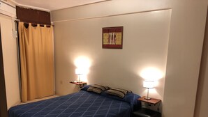 A bedroom with a blue bedspread, two bedside lamps, a small table, and a wall-mounted artwork. - Catalina Norte Centro (Tucuman)