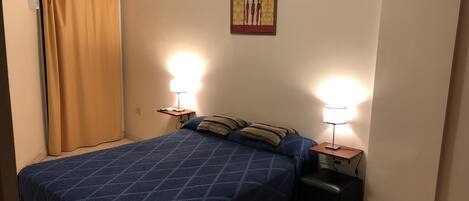 A bedroom with a blue bedspread, two bedside lamps, a small table, and a wall-mounted artwork.