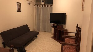 A living room with a sofa, a TV on a wooden stand, a chair, and an air conditioning unit. - Catalina Norte Centro (Tucuman)
