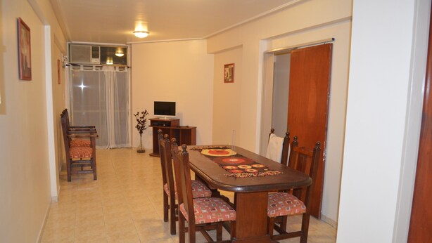 A dining area with a long wooden table, six chairs, and a television on a stand. - Catalina Norte Centro (Tucuman)