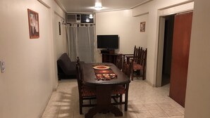 A dining area with a wooden table, chairs, a television, and a window with curtains. - Catalina Norte Centro (Tucuman)