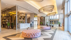 A spacious lobby with a central seating area, a reception desk, and a large window providing a view of the city.