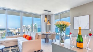 A modern living room with a sofa, dining table, and large windows offering a city view.