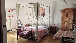 A bedroom with a four-poster bed, wooden flooring, a wooden wardrobe, and a bedside table with a lamp. - B&B Aria (Sarzana)