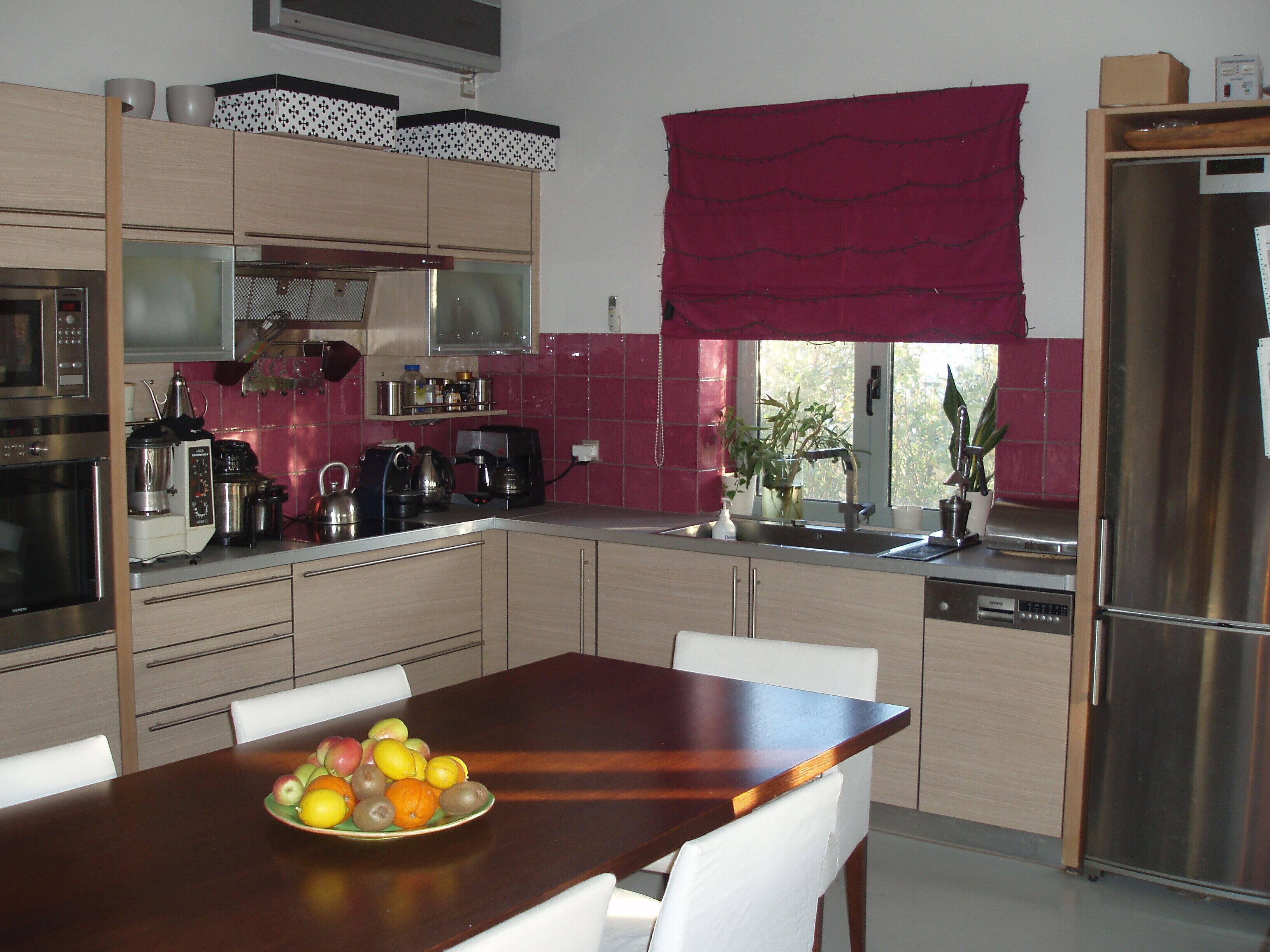 A modern kitchen with a wooden dining table, white chairs, and a fruit bowl.