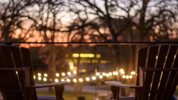 Eine Holzterrasse mit zwei Stühlen, die auf eine Geländer blicken, mit verschwommenem Blick auf Bäume und Lichter.