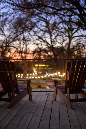 A wooden deck with two chairs facing a railing, overlooking a blurred view of trees and lights. - *The Blue Ridge* Container Home-Hot Tub | Fire Pit (Waco)
