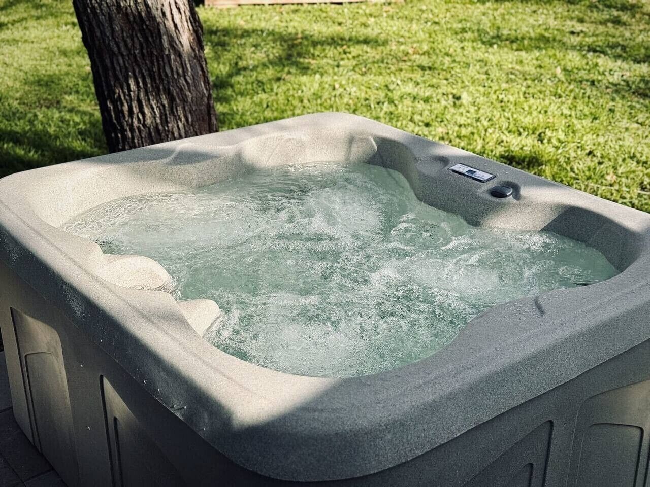 A hot tub with a control panel, surrounded by a grassy area.
