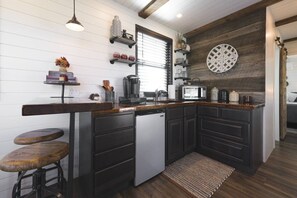 Una cocina con armarios oscuros, lavavajillas integrado, cafetera y microondas.
