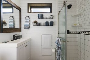 Un baño con tocador blanco, toallero, ducha con puerta de cristal y una pequeña ventana sobre el tocador.