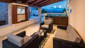 A cozy outdoor living area with wicker furniture, a TV, and a bar counter. - Villa Jasmine (Stari Grad)