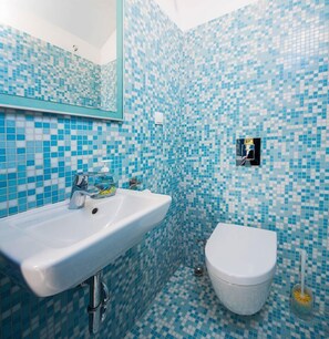 A bathroom with a white sink, a toilet, and a mirror. The walls and floor are tiled with blue and white mosaic tiles. - Villa Jasmine (Stari Grad)