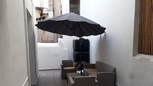 A small, enclosed outdoor seating area with wicker furniture and a black umbrella.