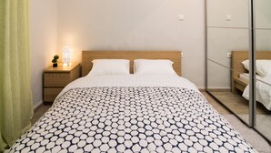 A neatly made bed with a patterned bedspread, a bedside table with a lamp, and a mirror on the wall.