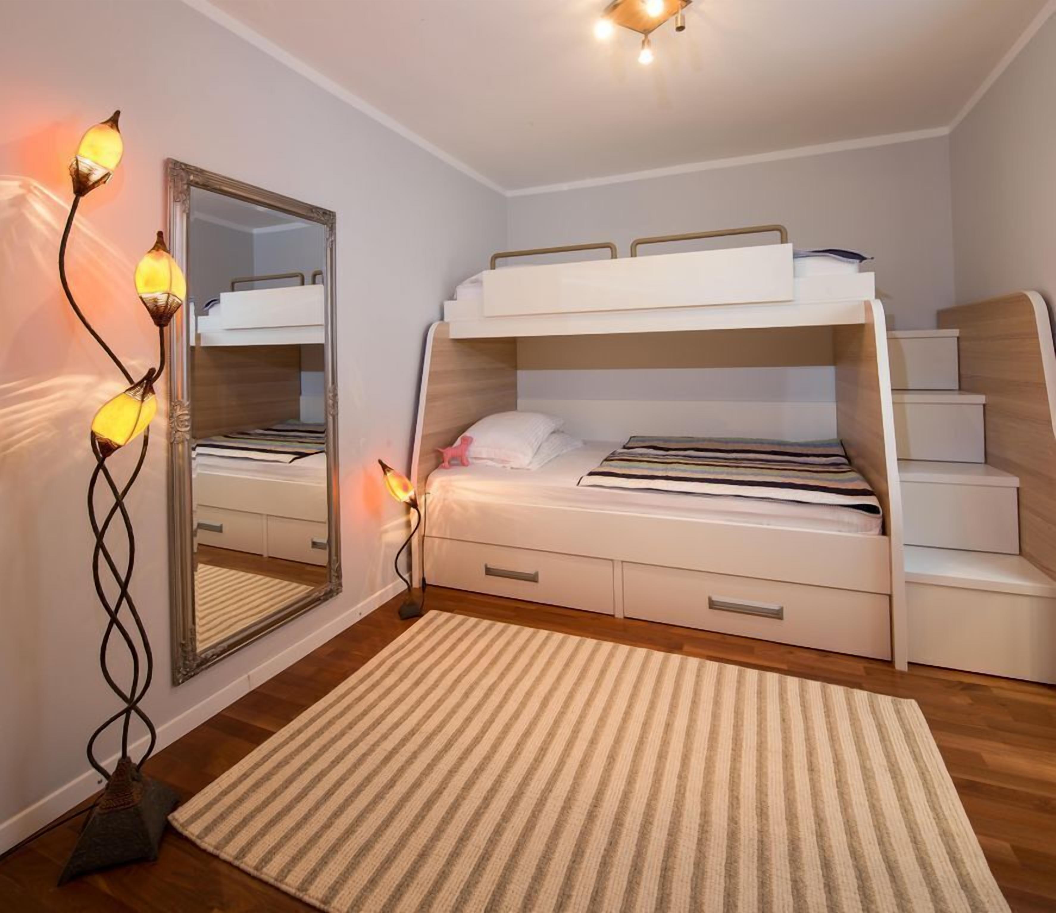 A bunk bed room with a mirror, bedside lamps, and a striped rug.