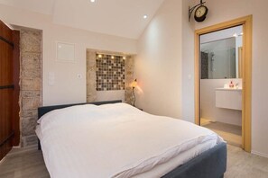 A bedroom with a bed, a stone wall, a clock, and a bathroom visible through an open door. - Holiday Home Secret Garden (Jelsa)