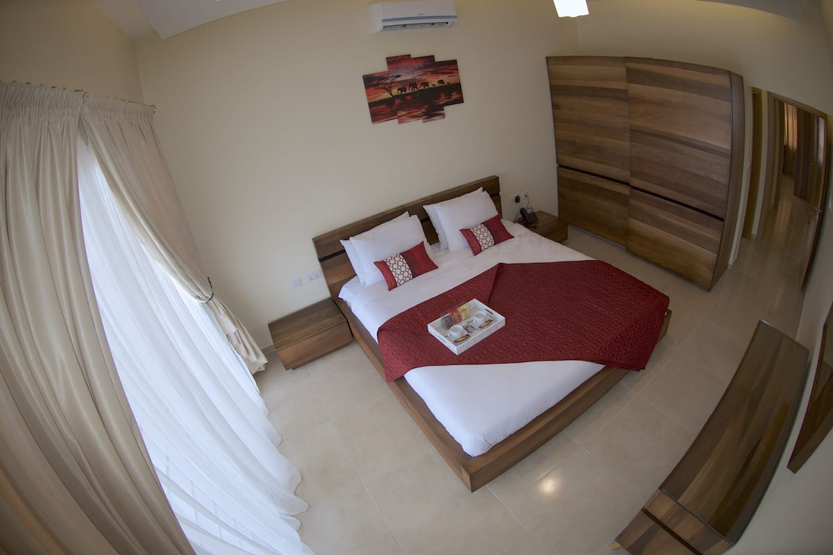 A bedroom with a bed, curtains, a bedside table, a nightstand, and a wall-mounted air conditioner.