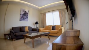 A living room with a sofa, armchair, and coffee table. There is a painting on the wall and a lamp. - Pearl Hotel & Residence (Freetown)