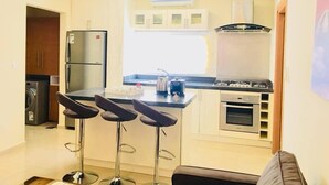 A compact kitchen with a refrigerator, stove, and bar stools. - Pearl Hotel & Residence (Freetown)