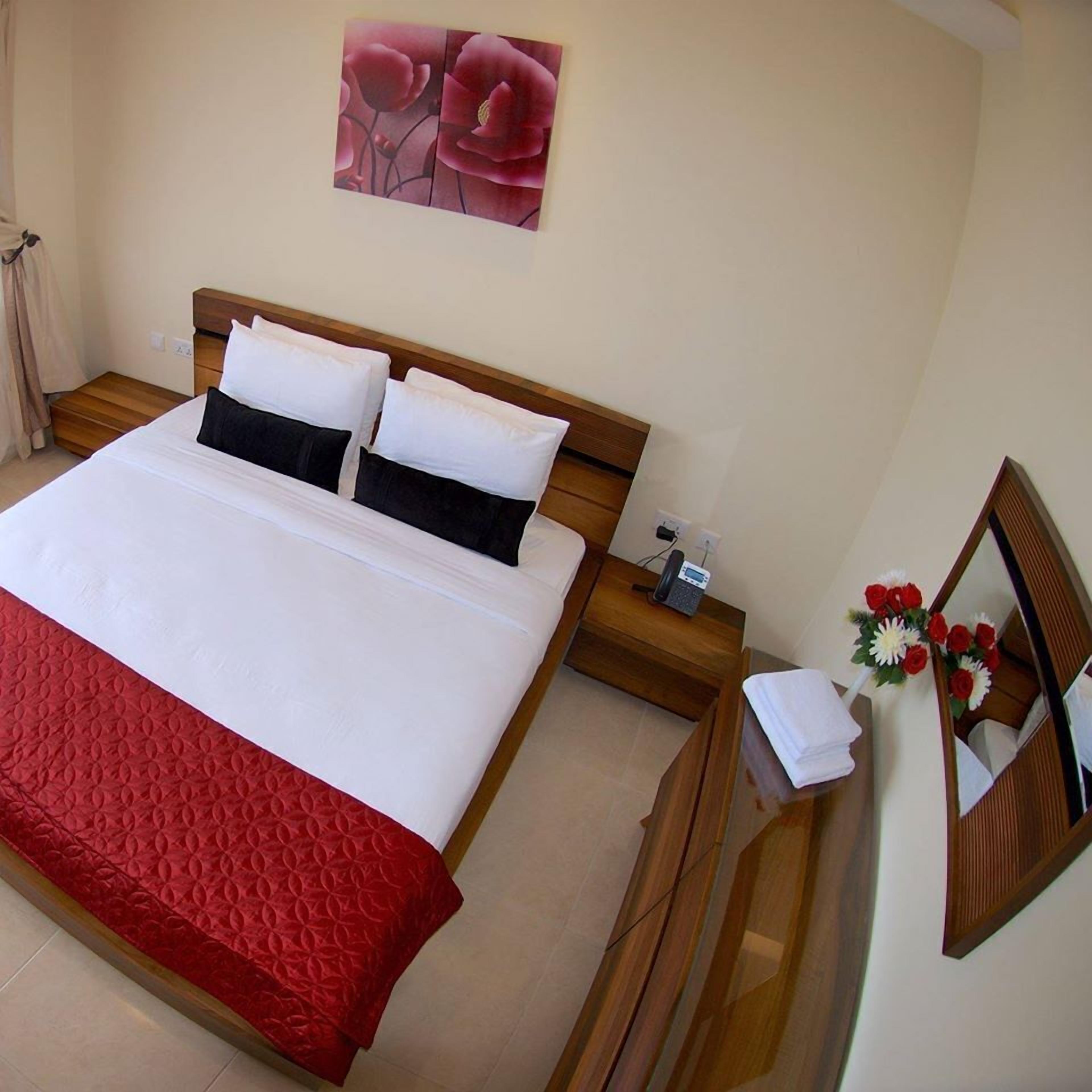 A hotel room with a large bed, a wooden nightstand, a telephone, and a mirror with a floral arrangement.