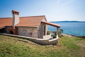 A stone house with a tiled roof, a chimney, and a small balcony overlooking a body of water.