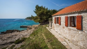 A stone building with red shutters by a coastal area. - Studio Zavala (Jelsa)