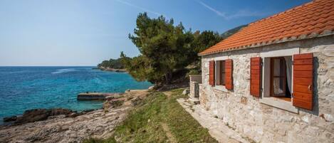 A stone building with red shutters by a coastal area.