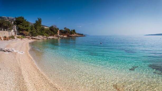 A beach with clear turquoise water, pebbly shore, and a building on the left. - Studio Zavala (Jelsa)