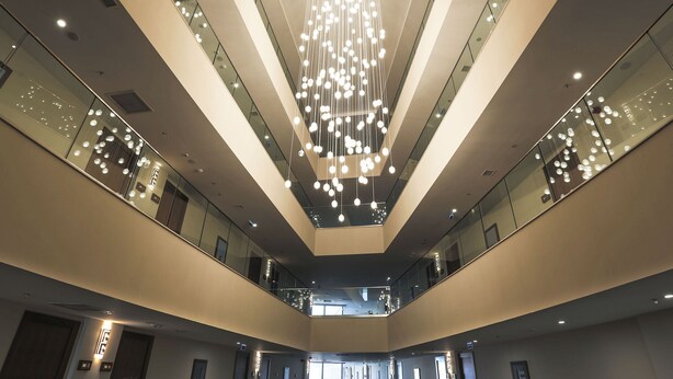 A modern interior with a central chandelier, glass railings, and a high ceiling. - Nevali Hotel (Sanliurfa)