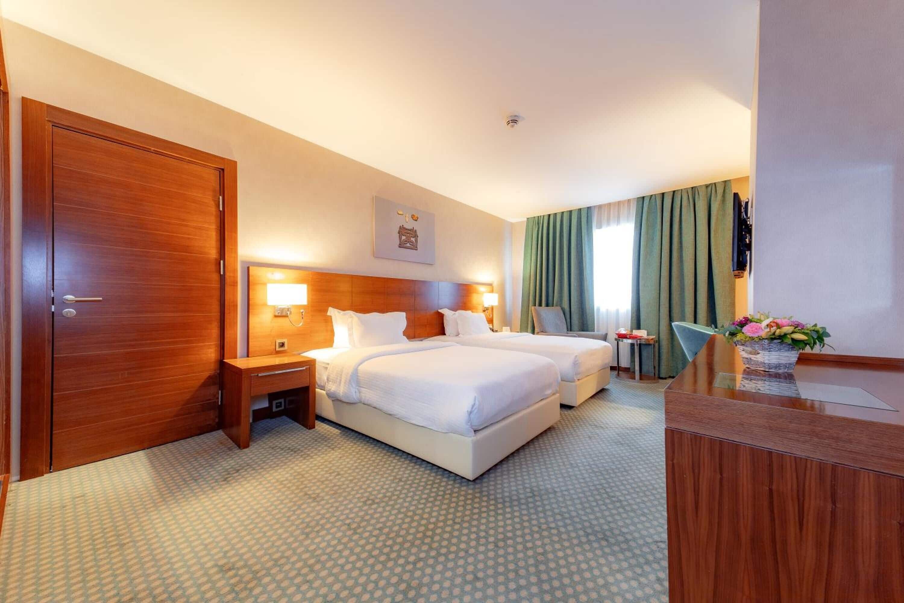 A hotel room with two beds, a desk, a chair, and a large wooden door.