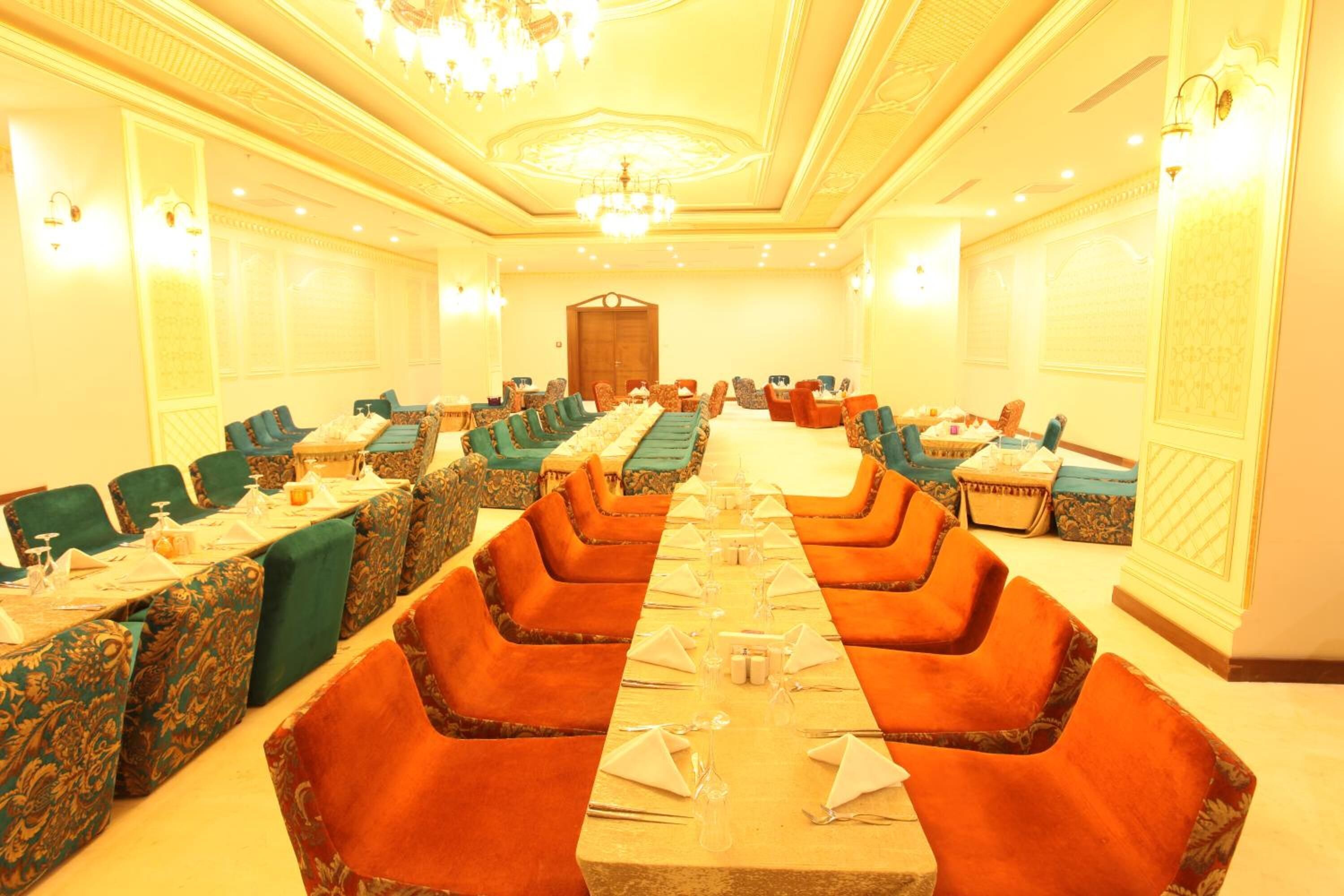 Un salón de banquetes con filas de mesas y sillas, una araña y decoraciones ornamentales en las paredes.