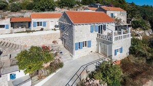 A stone building with a red-tiled roof, a balcony, and a staircase leading to the entrance. - Old Tree Villa (Jelsa)