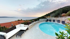 A curved pool with lounge chairs and a stone wall, overlooking a body of water and hills. - Old Tree Villa (Jelsa)
