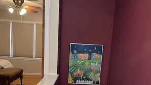 A staircase with a handrail, a wooden door at the bottom, and a painting of a farm scene on the wall.