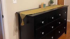 A hallway with a black dresser, a mirror with a geometric frame, a small plant, and a door.