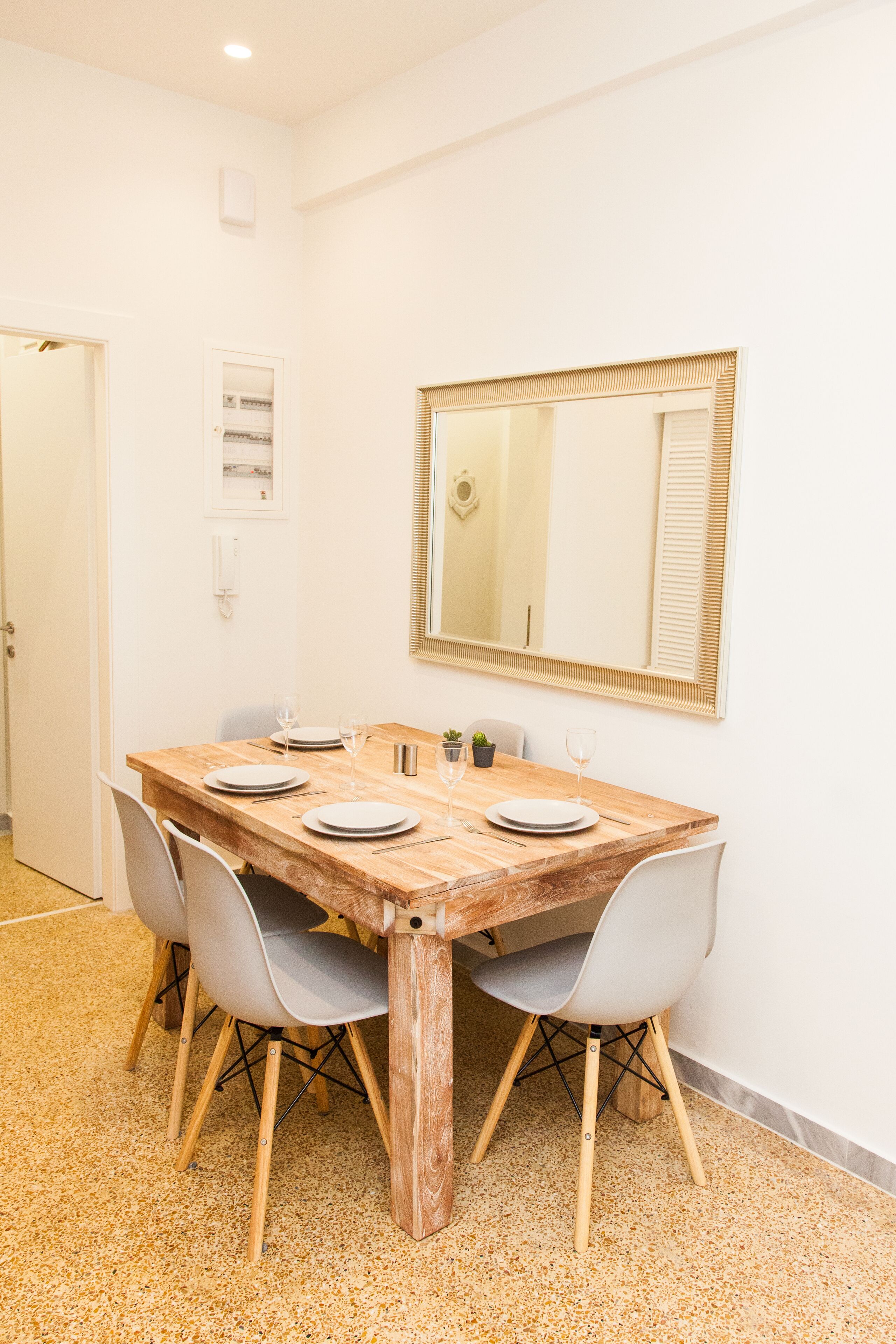 Een eethoek met een houten tafel, vier stoelen en een grote spiegel aan de muur.