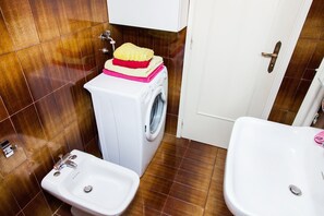 A compact bathroom with a washing machine, two sinks, and a door with a towel rack. - Calm Oasis Apartment in Marousi (Marousi)