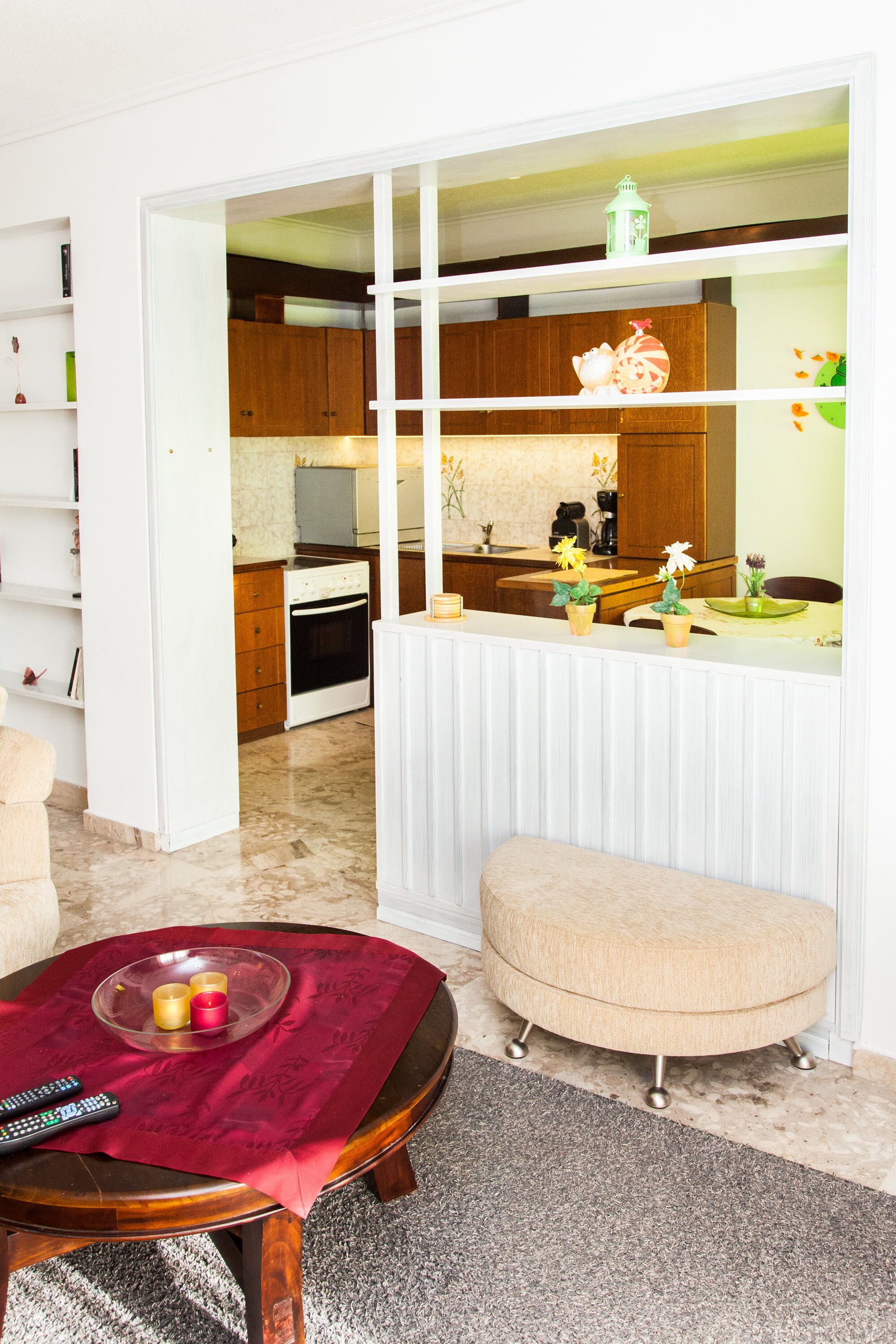 A modern kitchen with wooden cabinets, a white countertop, and a dining area with a red tablecloth.