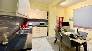 A compact kitchen with a microwave, sink, and a dining area with a table and chairs. - Chic Elegant New Apartment - Kolonaki (Athens)