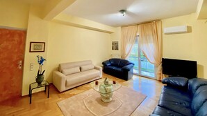 A living room with a beige sofa, a black leather sofa, a glass coffee table, and a flat-screen TV. - Chic Elegant New Apartment - Kolonaki (Athens)