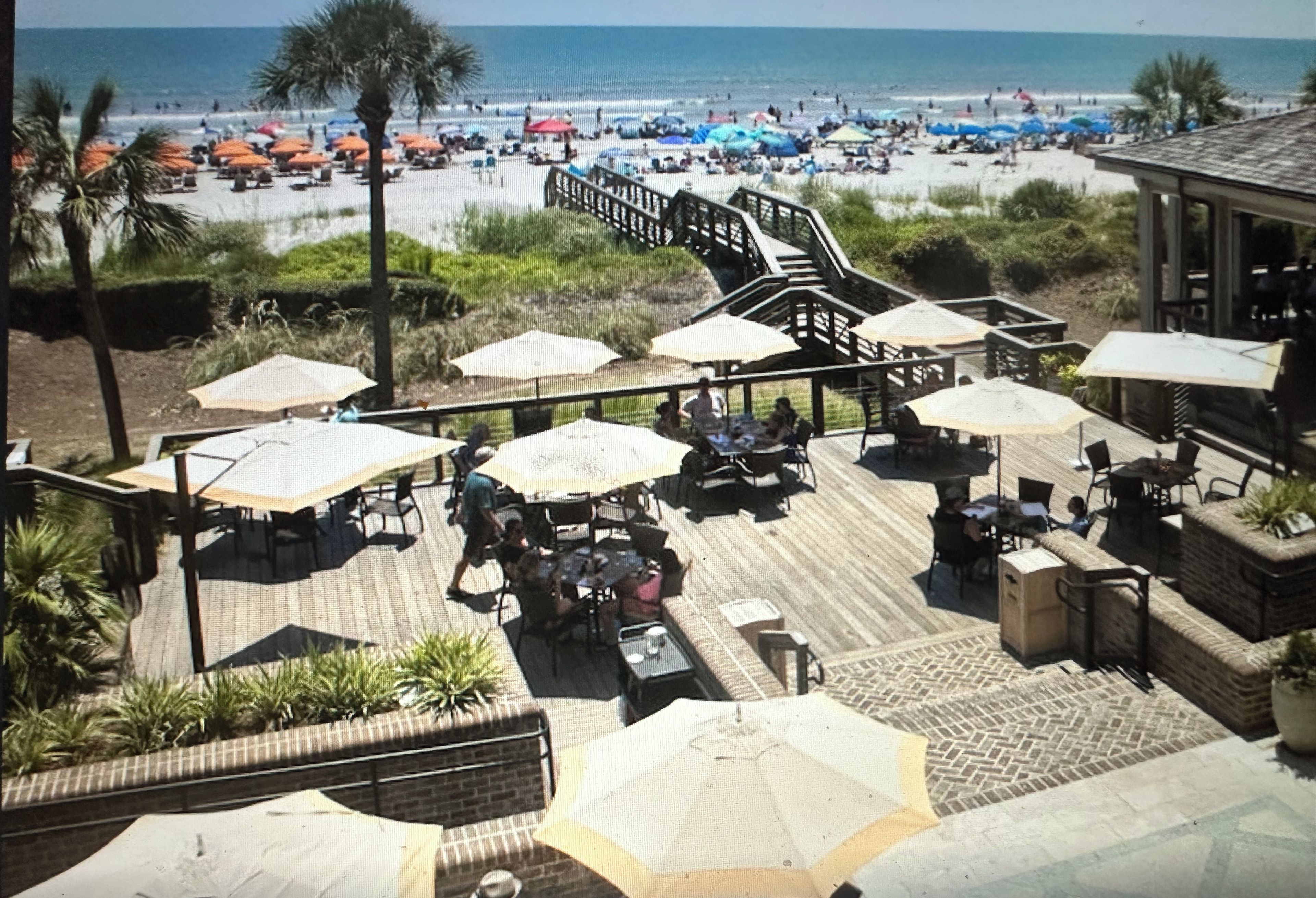 A beach club with outdoor seating, umbrellas, and a view of the beach.