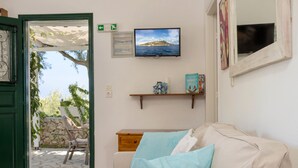 Ein gemütliches Zimmer mit einem beigefarbenen Sofa, einem an der Wand befestigten Fernseher und einem kleinen Regal mit Dekoration.