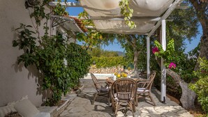 Eine Terrasse mit Steinboden, Korbstühlen und einem Tisch mit Blumen in einer Vase.