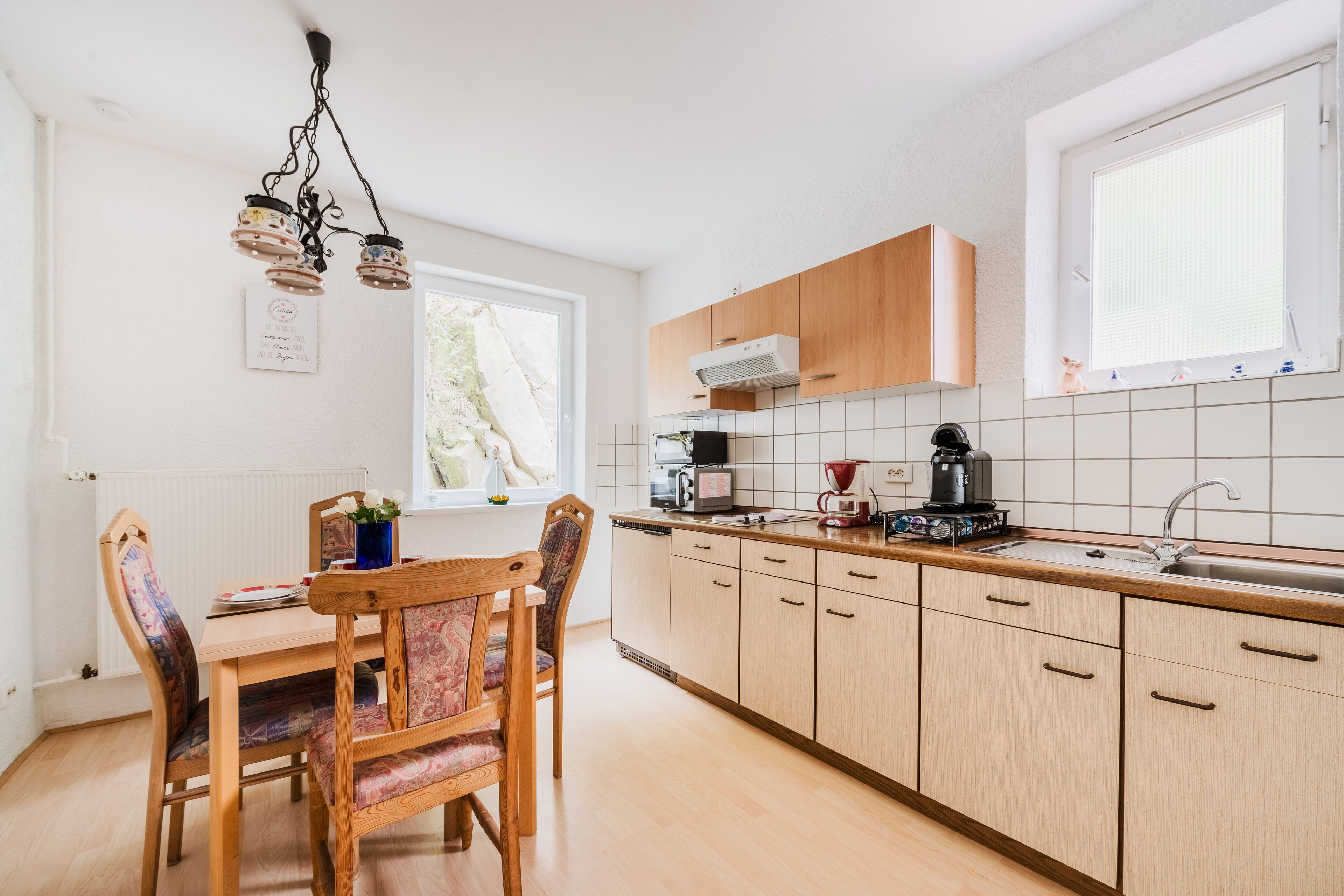 A modern kitchen with wooden cabinets, a dining table with chairs, a hanging light fixture, and a window providing natural light.