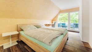 Un dormitorio con techo inclinado, una cama de madera, un escritorio y vistas al exterior.
