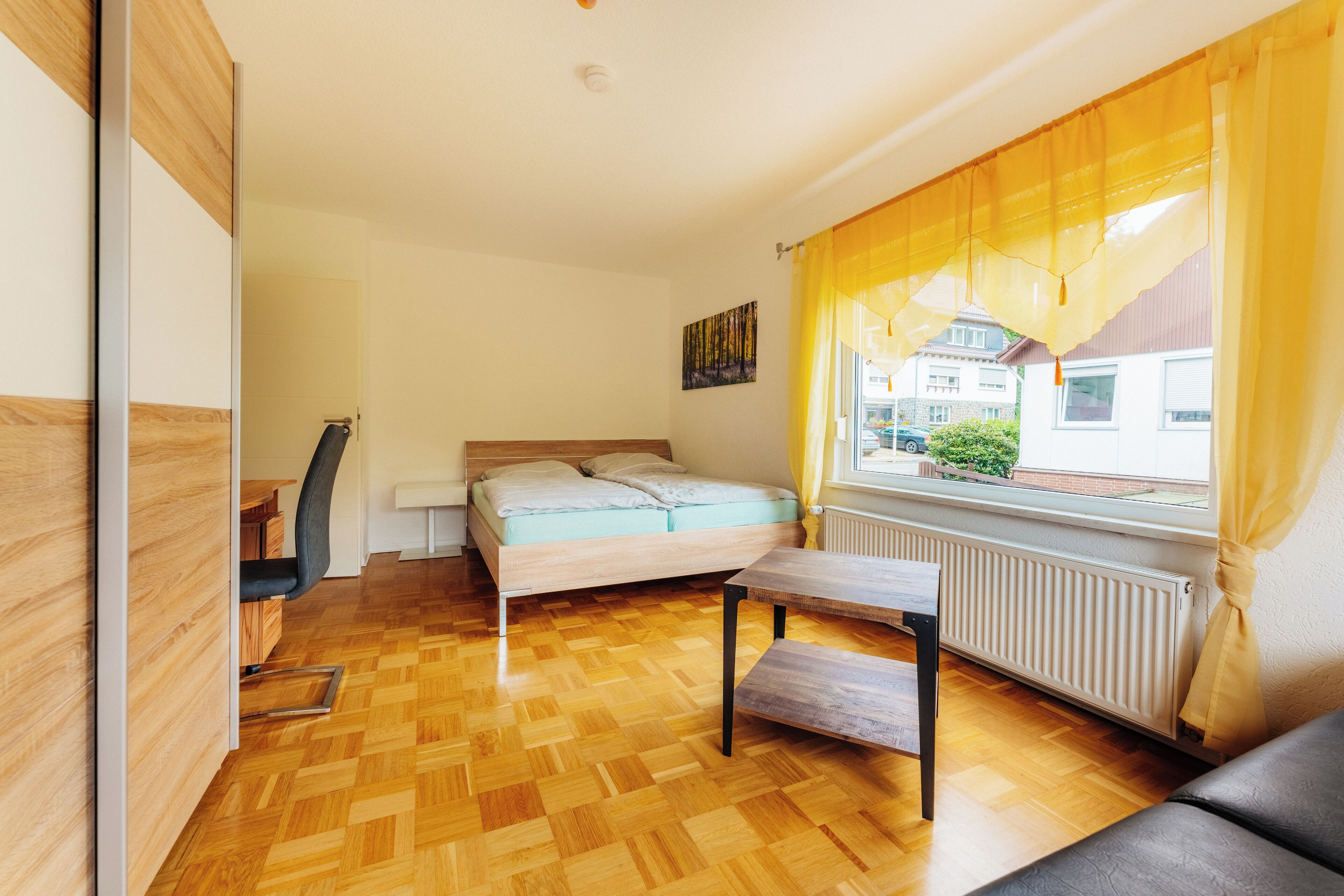 A bedroom with a bed, a desk, a chair, and a window with curtains.