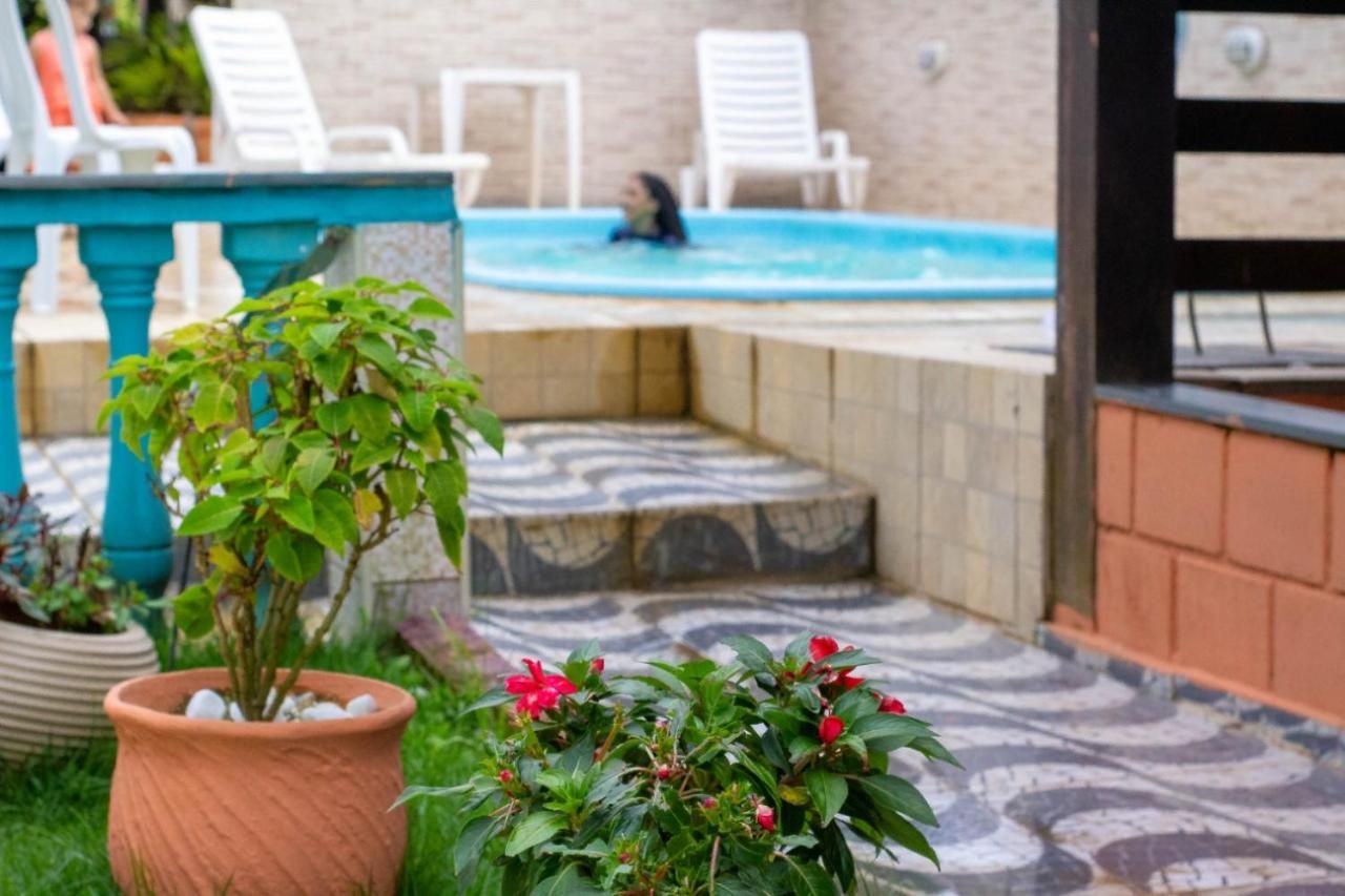 Área da piscina com degraus para entrar na água, cercada por plantas em vasos e mobiliário de exterior.