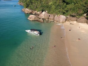 Ein Boot vor Anker in der Nähe eines Strandes mit großen Felsen und einem bewaldeten Ufer im Hintergrund.