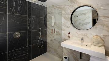 A modern bathroom with a walk-in shower, a round mirror, a white sink, and a towel rack.